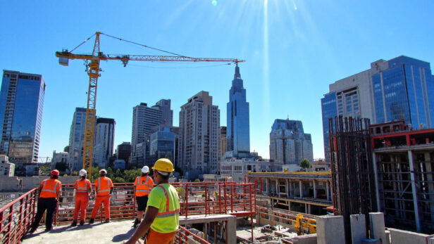 Construction site in Texas with workers in safety gear and modern skyscrapers in the background under bright sunlight.