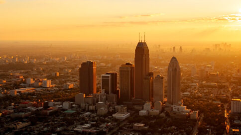 Aerial view of a Texas cityscape showing construction cranes and modern skyscrapers during a golden sunset.