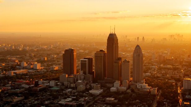 Aerial view of a Texas cityscape showing construction cranes and modern skyscrapers during a golden sunset.