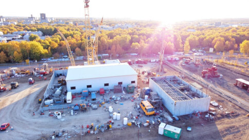 Aerial view of a construction site with a drone capturing imagery of workers and equipment below.