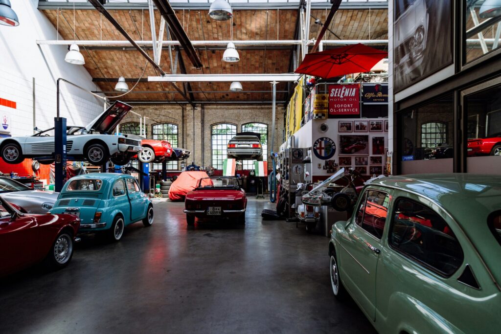 Vintage cars are arranged inside a spacious, well-lit automotive workshop.