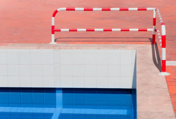 A swimming pool with vibrant blue water and red-white safety barriers.