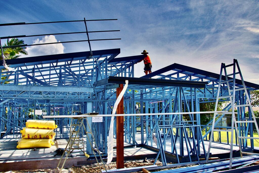 Construction worker on roof of a blue steel-framed building under a clear sky.