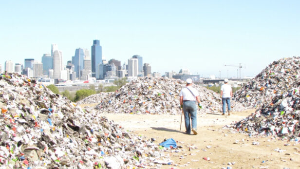 Construction site with recycled materials, workers in hard hats, and Texas skyline in background under bright sunlight.