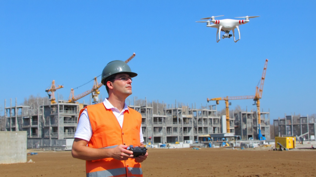 Construction Worker Surveying Building Site with Drone Construction worker operating a drone controller, surveying a large building site with scaffolding and cranes.