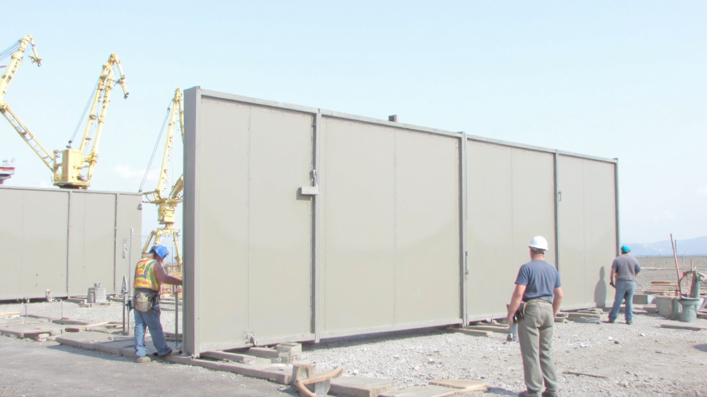 Construction Workers Assembling Prefabricated Wall Panels Construction workers assembling large prefabricated wall panels on a building site with cranes in the background.