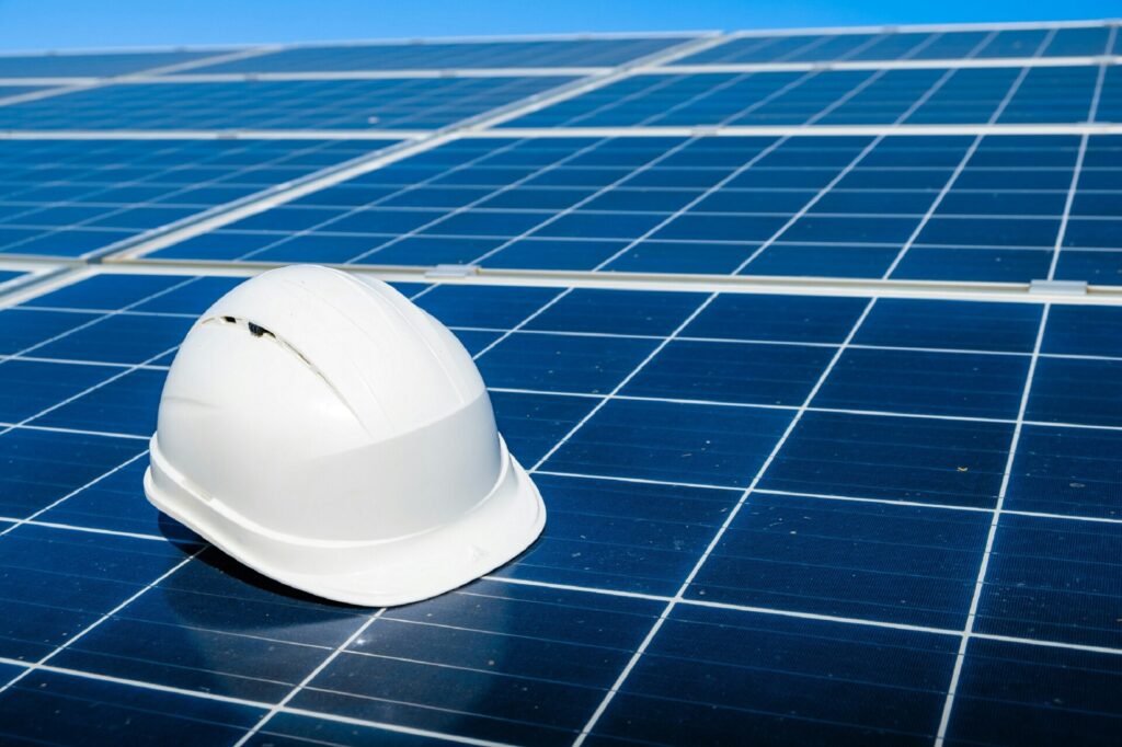 A white hard hat rests on a field of blue solar panels under clear skies.