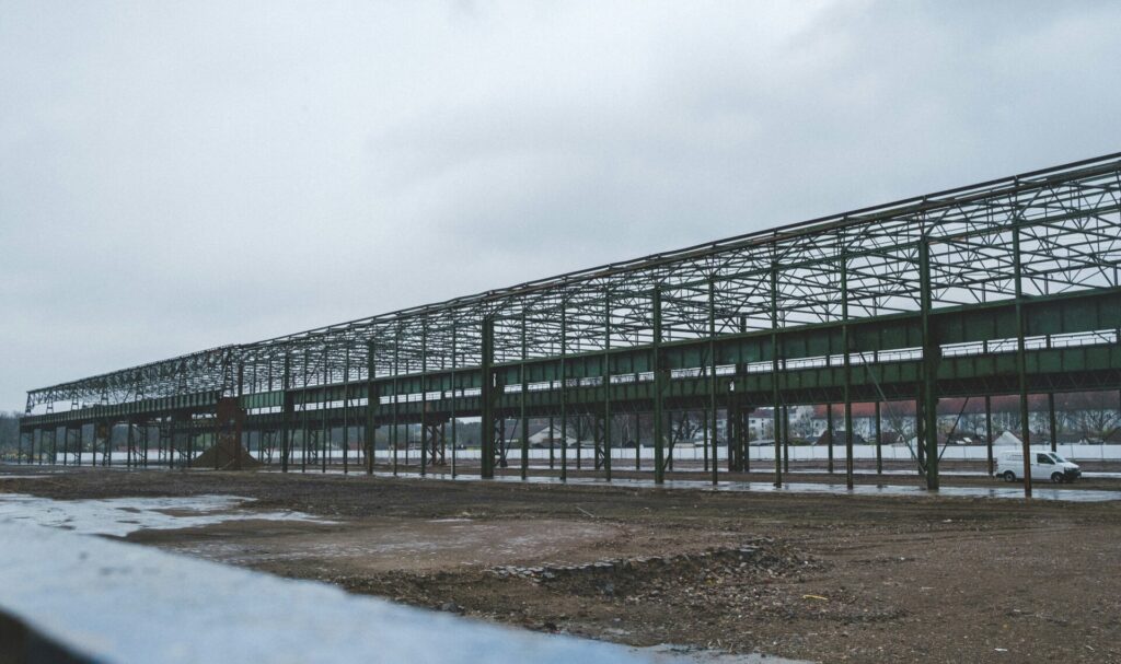 Large green metal frame structure in an empty area under a cloudy sky.