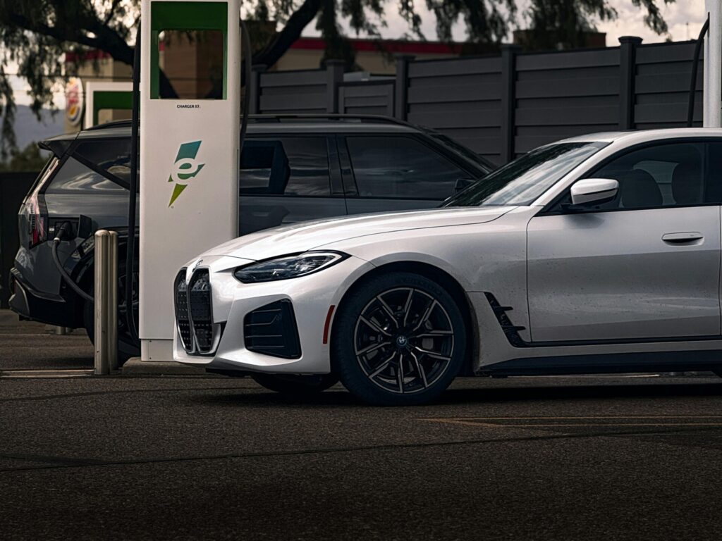 A white electric car charges at a public charging station in a parking area.