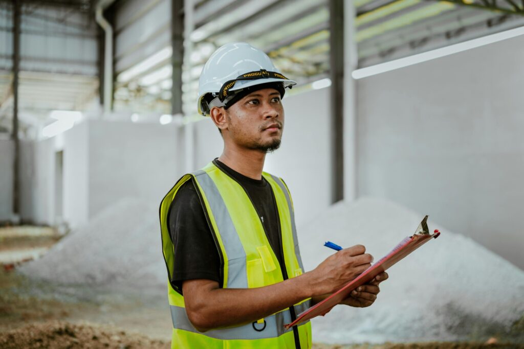 Construction worker in a hard hat and vest takes notes on a clipboard.