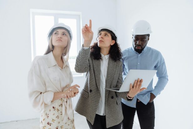 Three engineers in hard hats discuss plans in a bright, empty room.