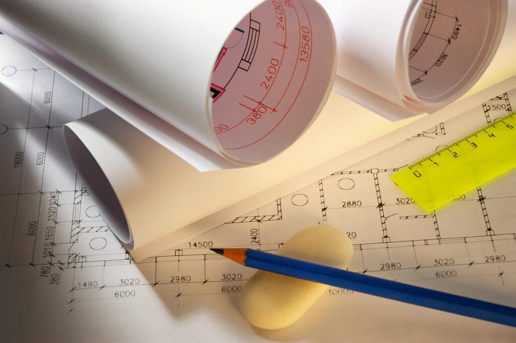 Rolled and flat blueprints with a pencil, eraser, and ruler on a table.