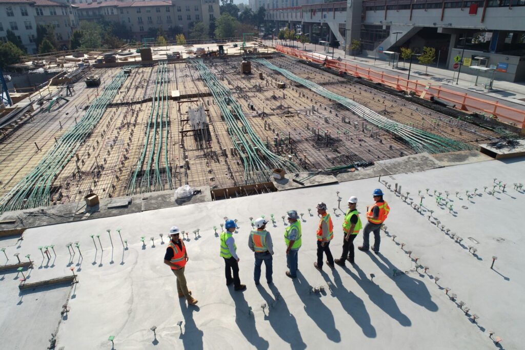 Construction workers in safety gear inspect a large building site with rebar.