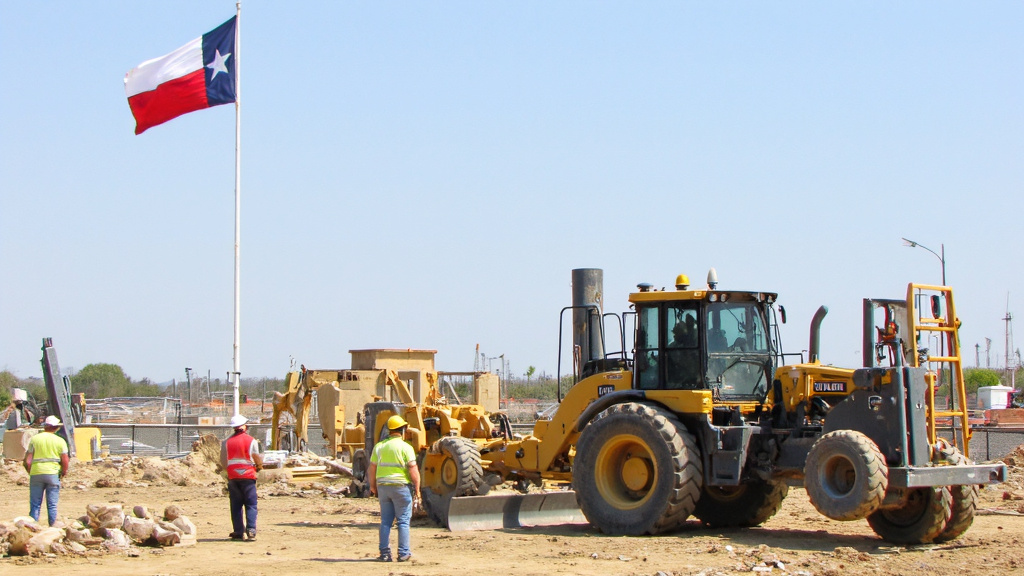 Texas Flag at Construction Site Texas flag waving near a modern construction site with workers and robots working side by side