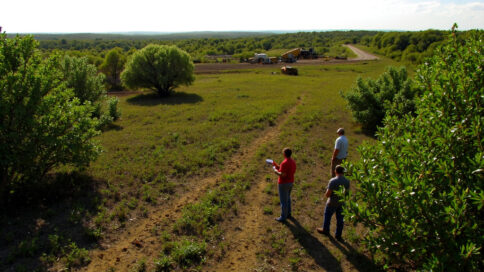 Aerial view of a Texas construction site with lush green areas surrounding and environmental scientists surveying the land.