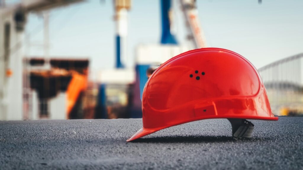 A red construction helmet rests on a flat asphalt surface at a site.