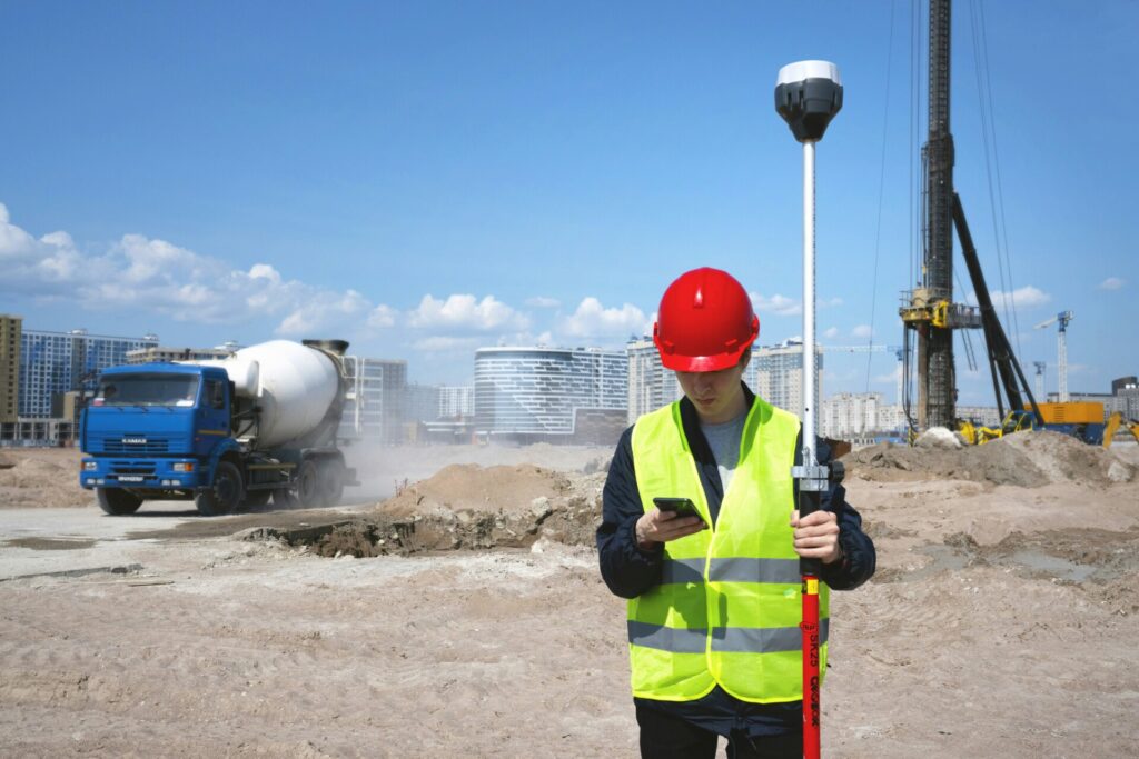 Construction worker with hardhat and reflective vest uses equipment on a building site.