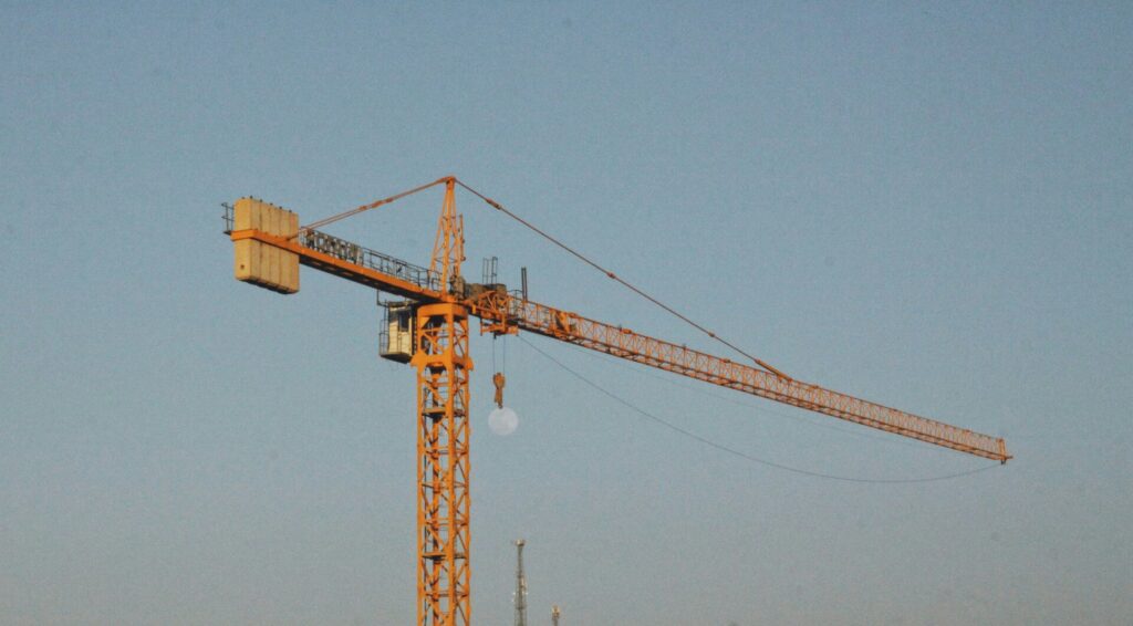 A large construction crane appears to be holding the moon in the sky.