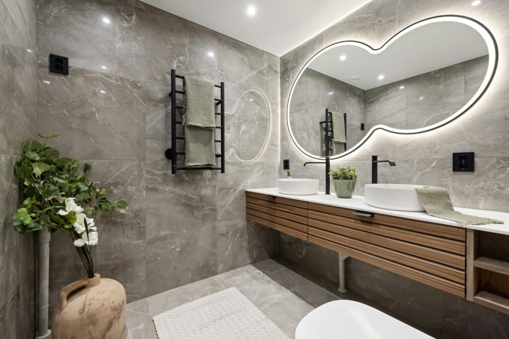 Modern bathroom with double sinks and an irregularly shaped backlit mirror.
