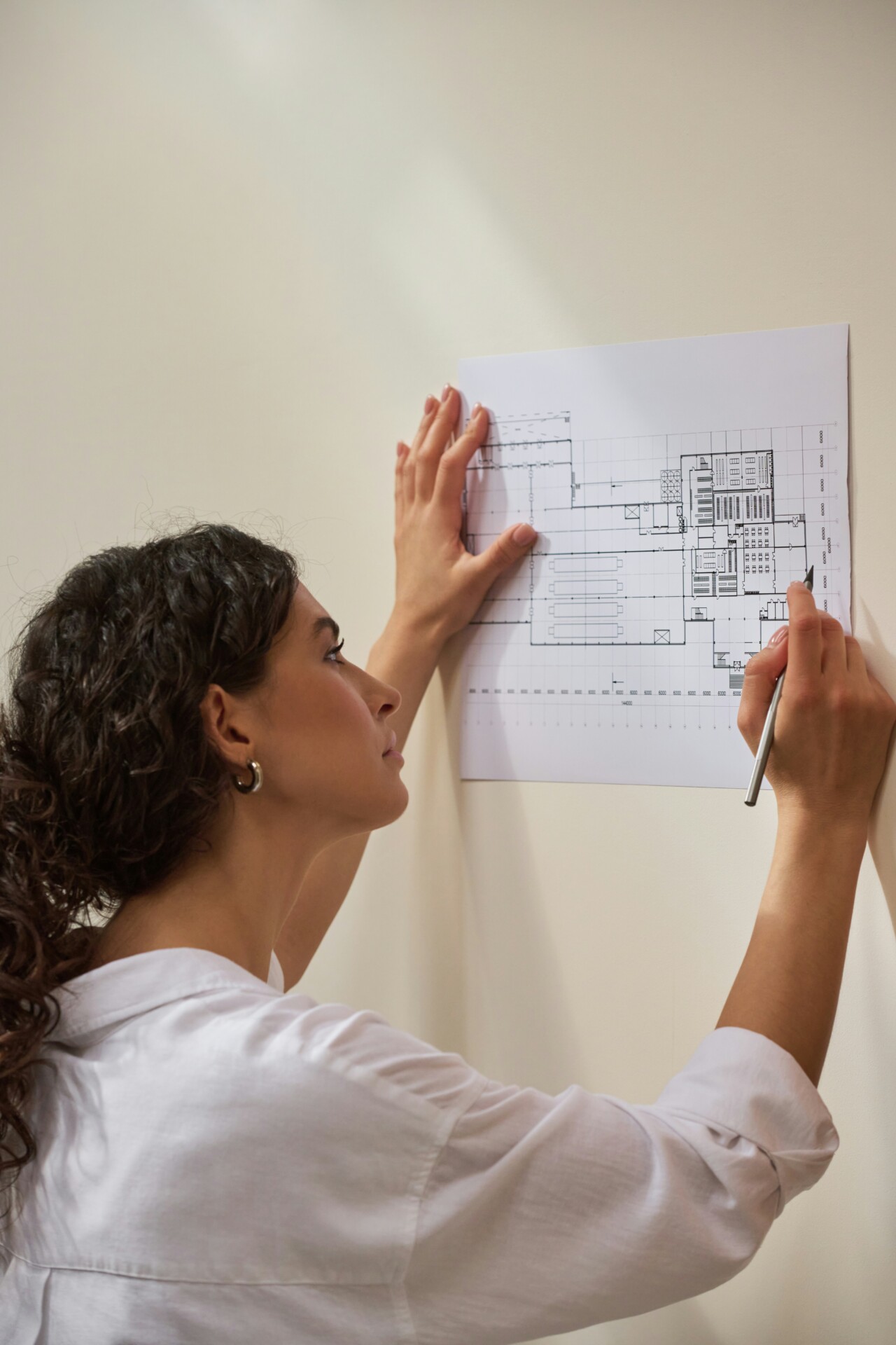 Creative Architectural Planning A woman sketching on a floor plan against a neutral wall.