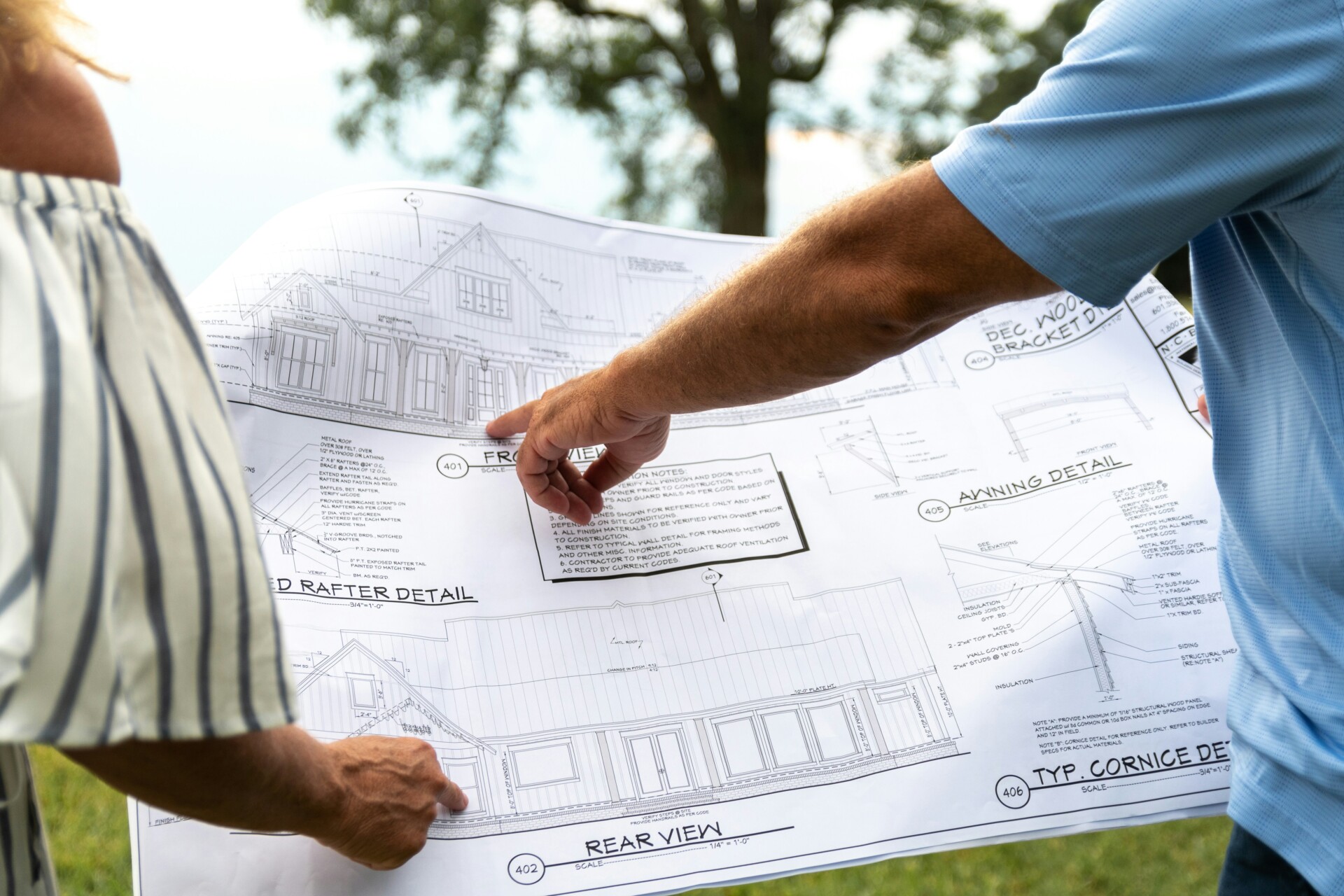 Discussion on Architectural Blueprints Two people discussing architectural blueprints outdoors.