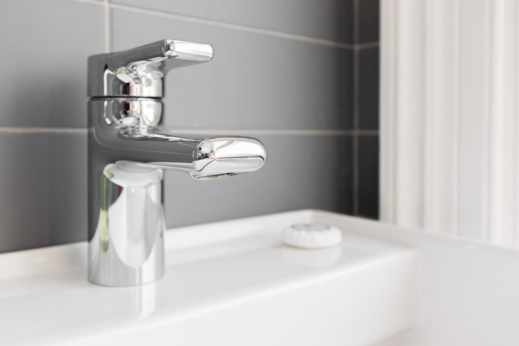 A modern chrome faucet on a white ceramic sink in a bathroom.