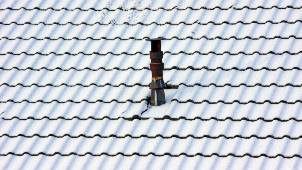 A snow-covered roof with a single chimney protruding through the tiles.