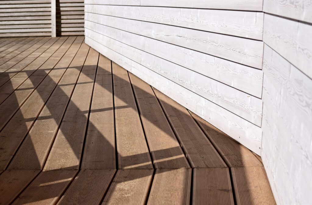 Sunlight casts geometric shadows on a wooden deck with white paneled walls.
