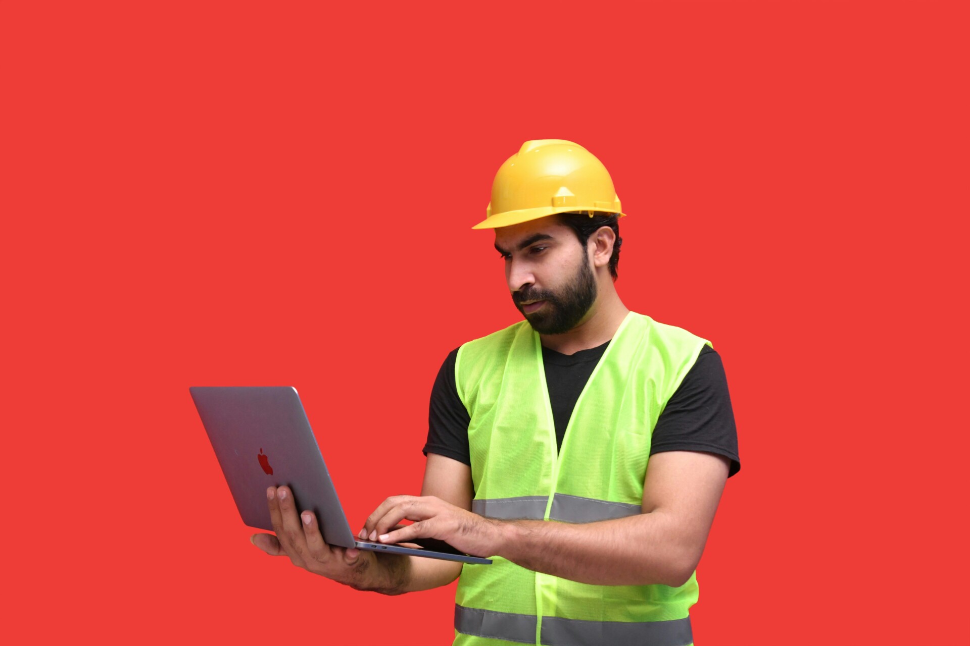 Construction Worker Engaged with Technology A construction worker in a yellow safety helmet and green reflective vest using a laptop.