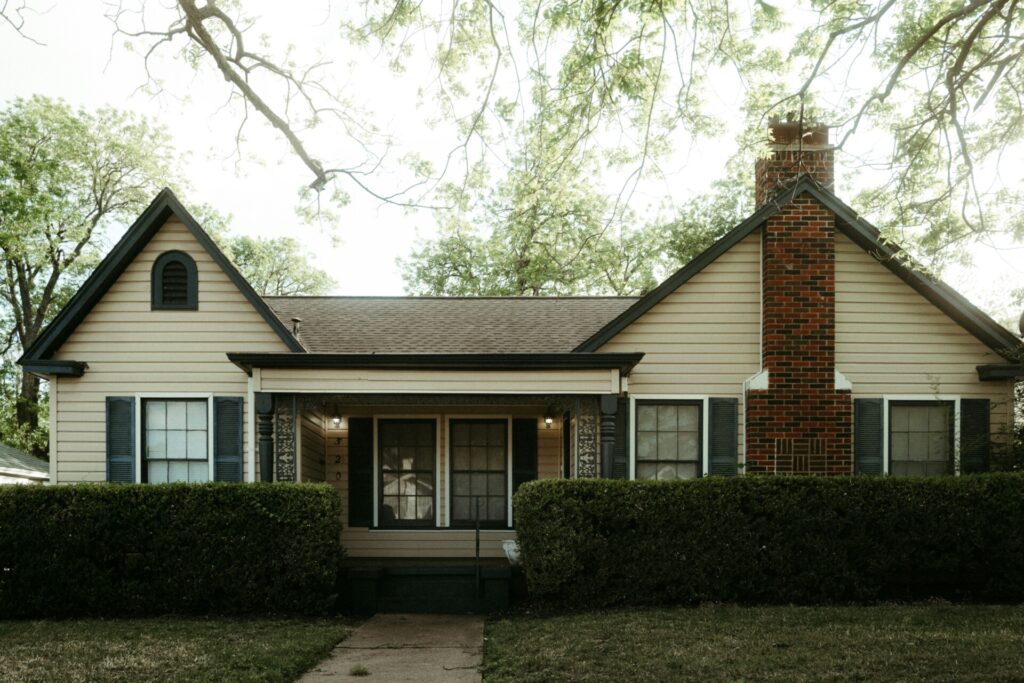A cozy suburban house with a brick chimney surrounded by greenery.