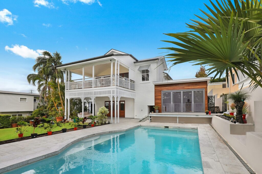 Modern white house with wooden accents and a swimming pool in the foreground.