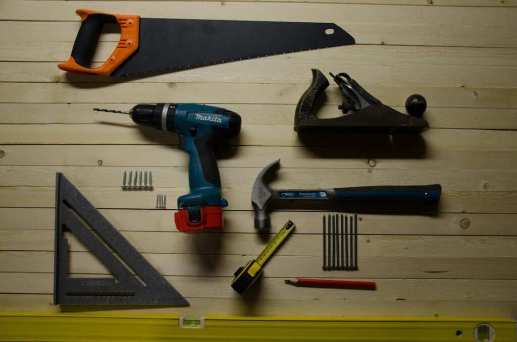 A selection of hand tools and a power drill arranged on a wooden surface.