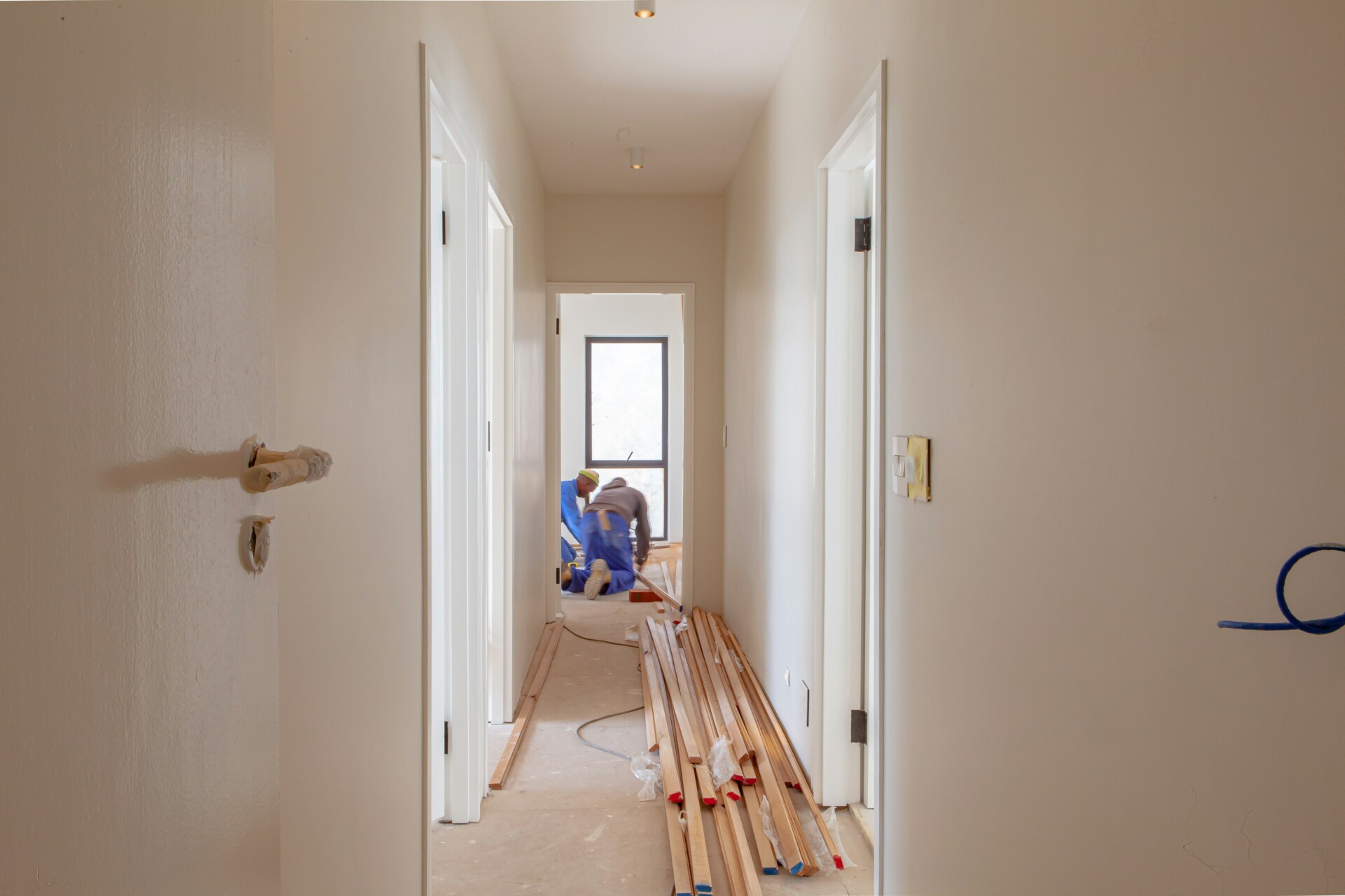 Renovation in Progress: Hallway Transformation View of a hallway under renovation with wooden planks on the floor and construction workers in the background.