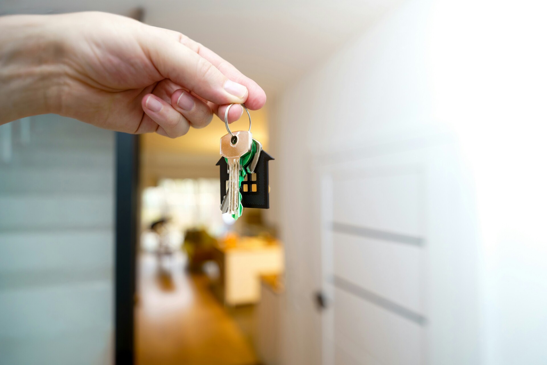 A hand holding a set of house keys with a keychain shaped like a house.