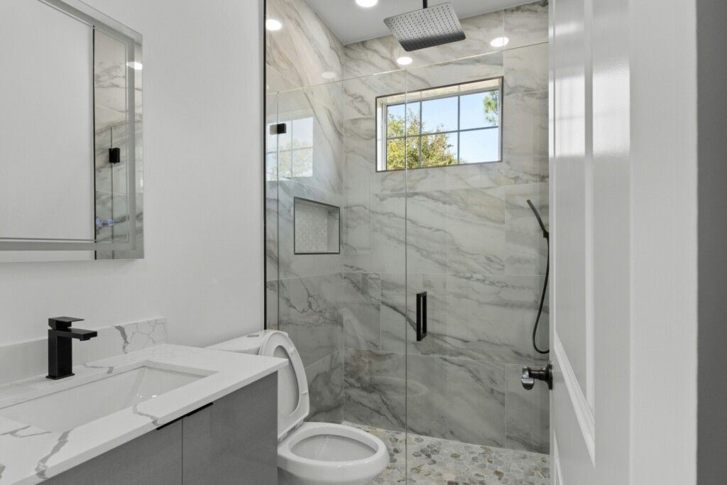 A modern bathroom featuring a glass shower, marble walls, and a sleek sink.