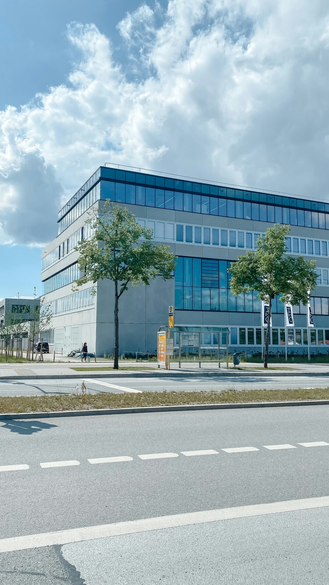 A modern building with large glass windows and trees in front under a cloudy sky.