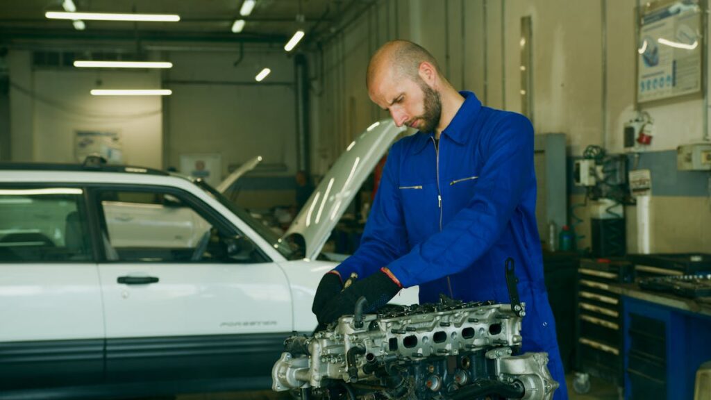 A mechanic in blue overalls works on an engine in a garage.