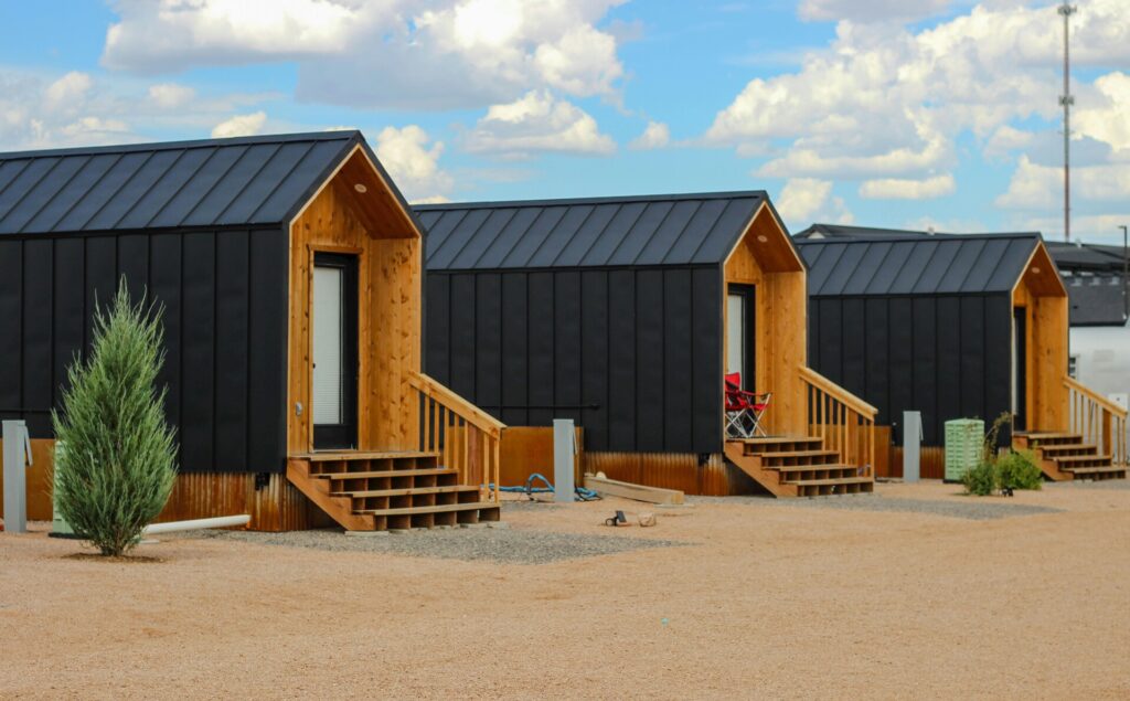 Row of modern tiny homes with wooden accents and metal roofs under a blue sky.