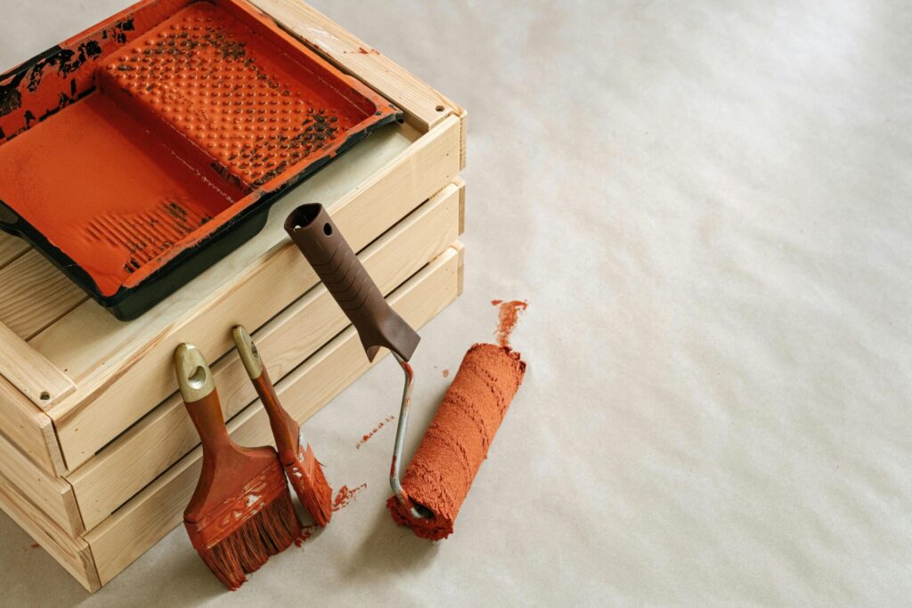 Painting tools with orange paint on a wooden crate and paper background.
