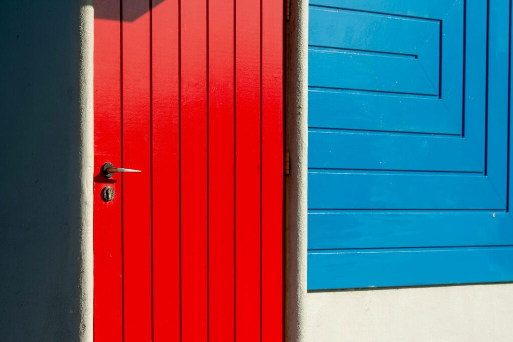 A bright red door next to a vibrant blue wall in sunlight.