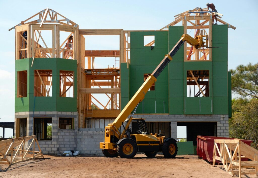 Construction site with a partially built house and a yellow telescopic handler.