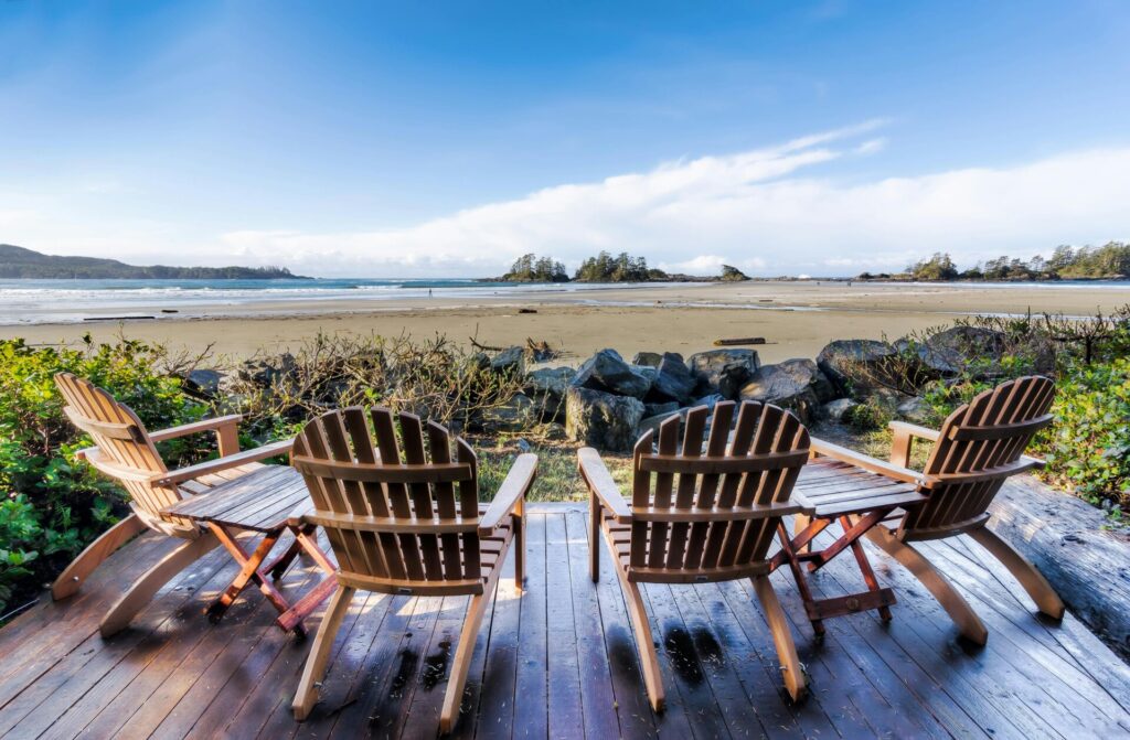 Four wooden chairs overlook a sandy beach with a clear blue sky.