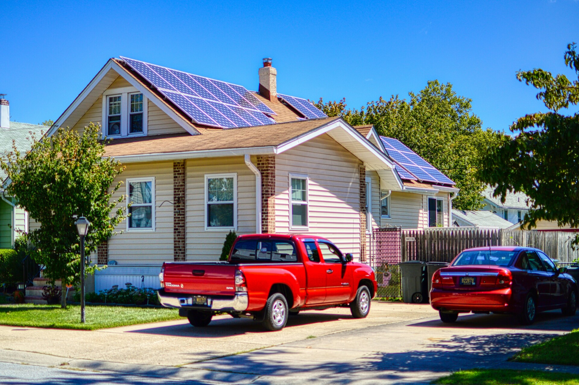 Eco-Friendly Home with Solar Energy A residential home featuring solar panels on the roof, surrounded by greenery and parked cars.