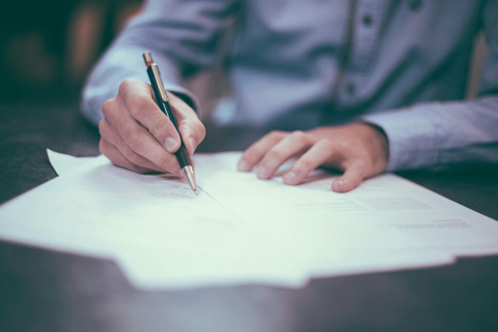 A person writing on documents with a pen at a desk.