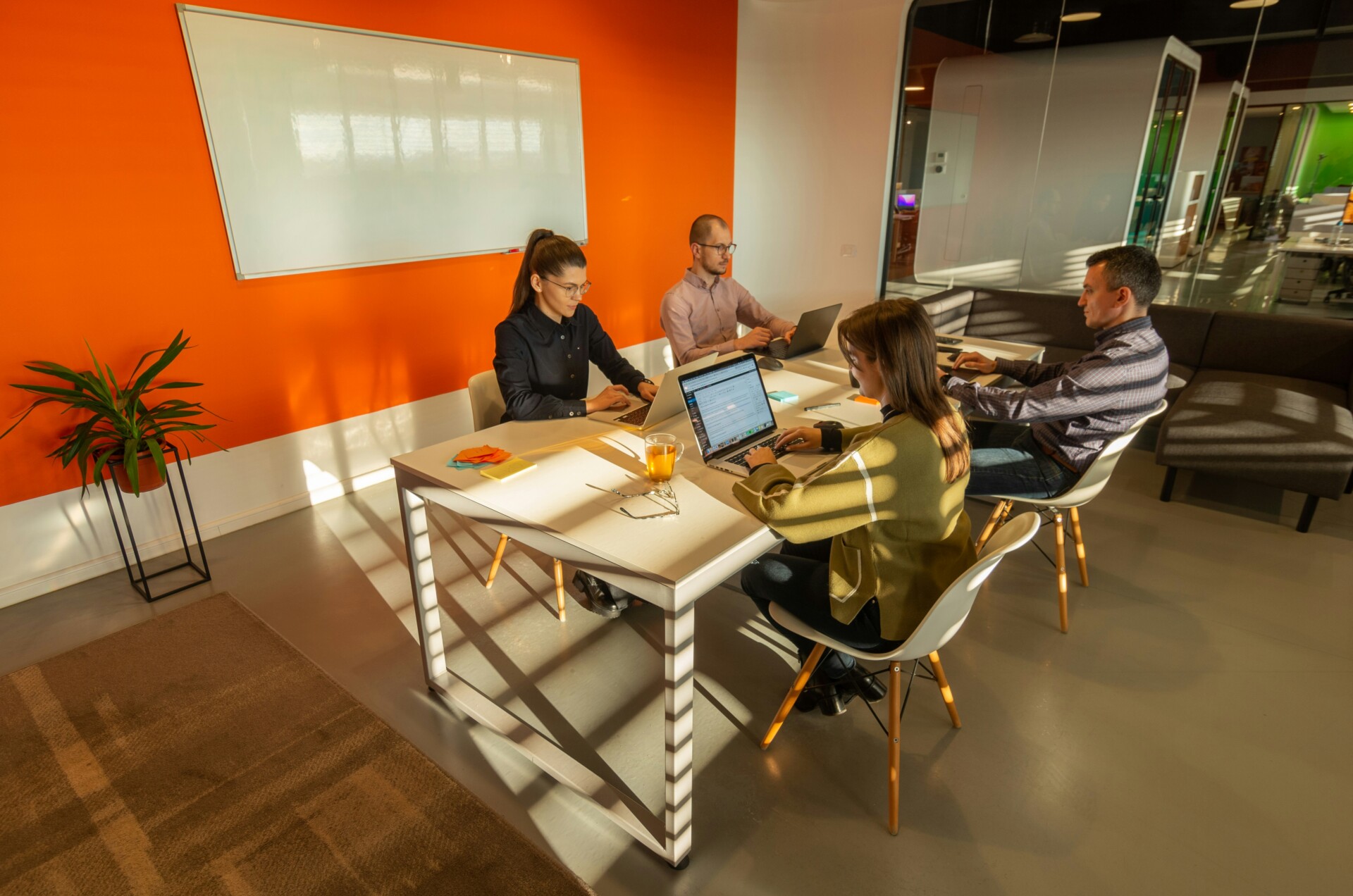 Collaborative Team Meeting in a Modern Office A group of four professionals collaborating around a white table in a vibrant orange-walled meeting room.