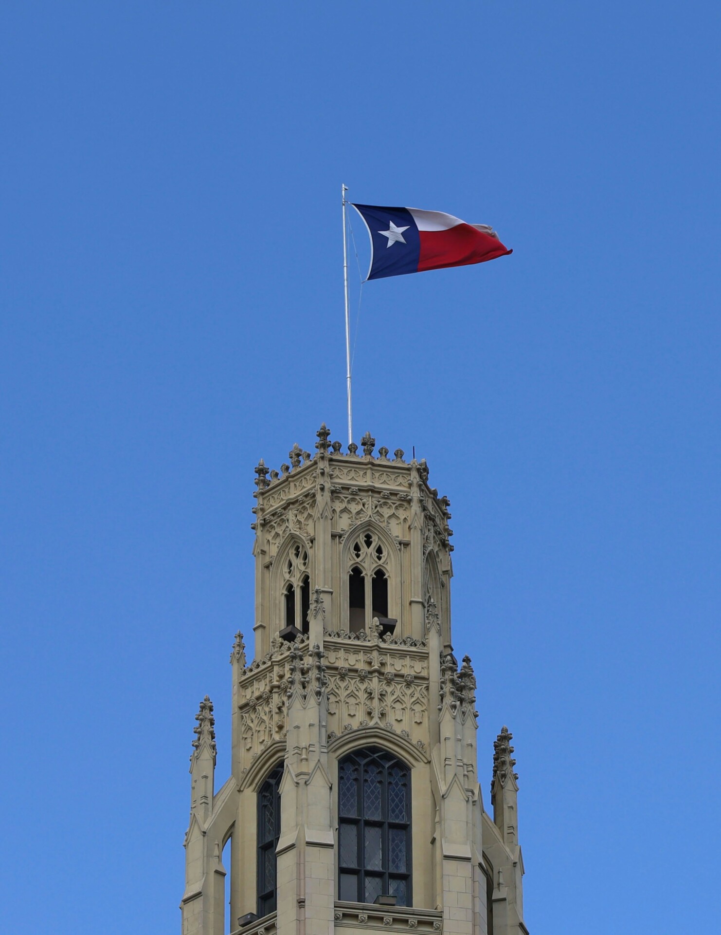 Texas Flag on Historic Building Texas flag waving atop a historic building tower against a clear blue sky.