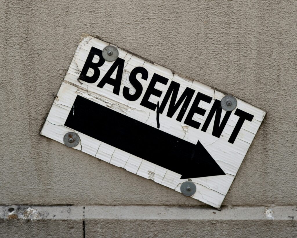 A weathered sign indicates the direction to a basement with a black arrow.