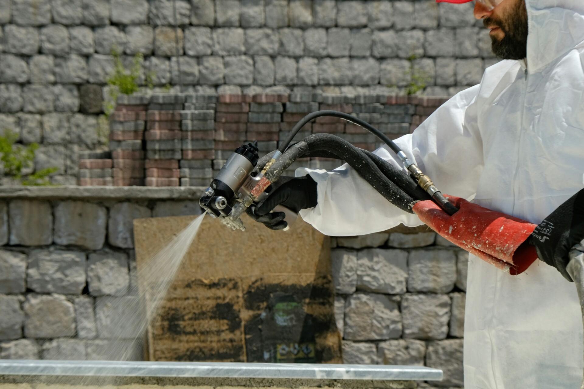 Waterproofing Application in Progress A person wearing protective gear uses a spray nozzle for waterproofing on a construction site.