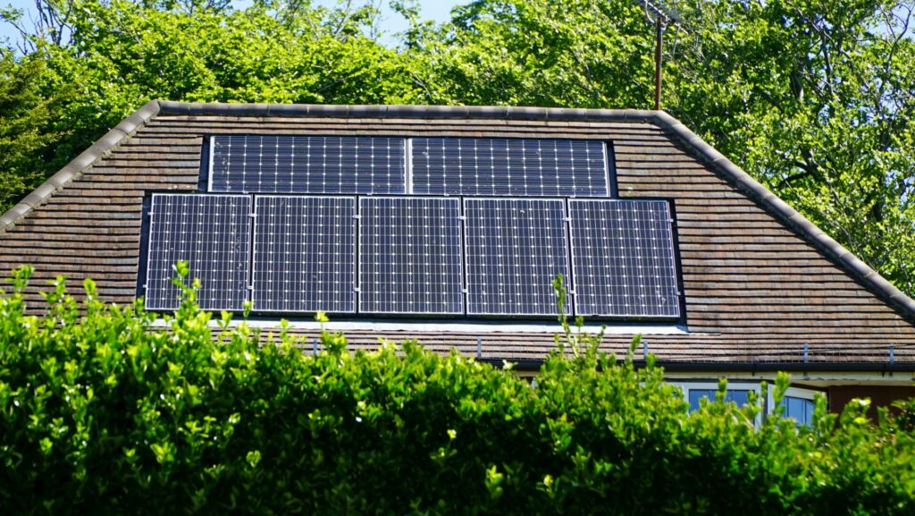 Solar panels installed on a house roof surrounded by lush green foliage.