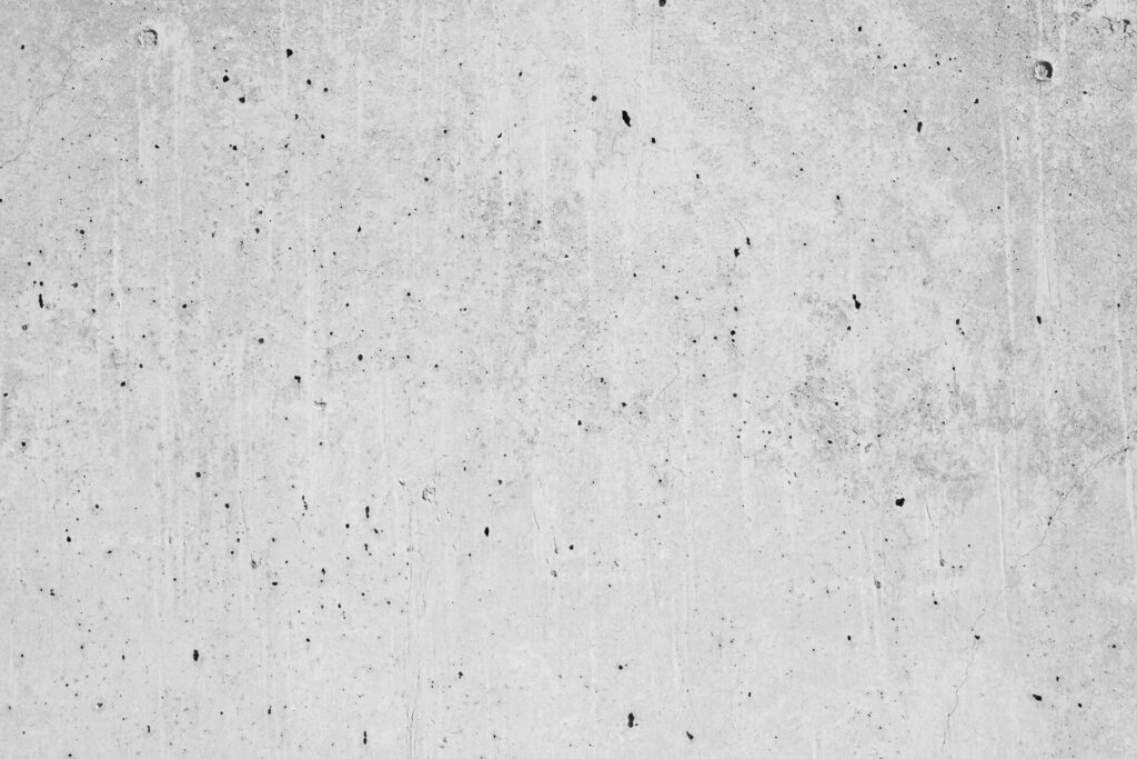 A textured concrete wall with small cracks and dark speckles.
